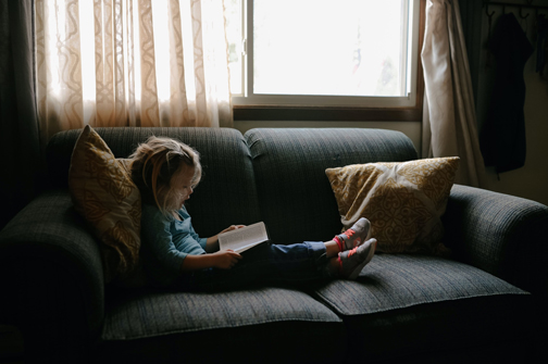 Little girl on a couch reading a Bible